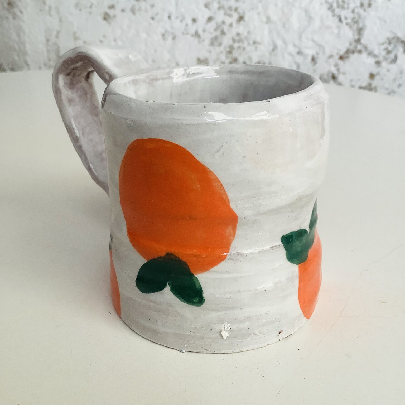 hand thrown white mug with large hand painted orange with green leaf. Made on a potter's wheel at eastnor pottery by a course participant