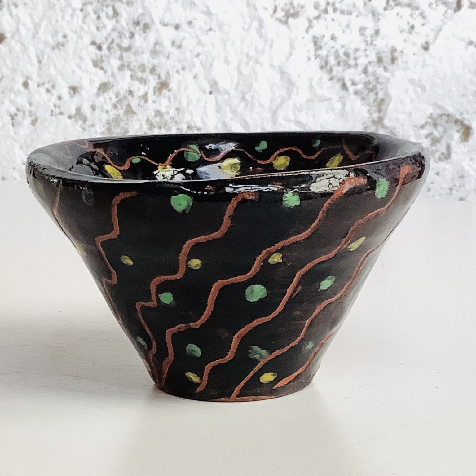 hand thrown bowl the shape of a truncated inverted cone. Black glaze with diagonal red zigzaged lines travelling from bottom to top. spaces inbetween lines punctuated with teal dots.