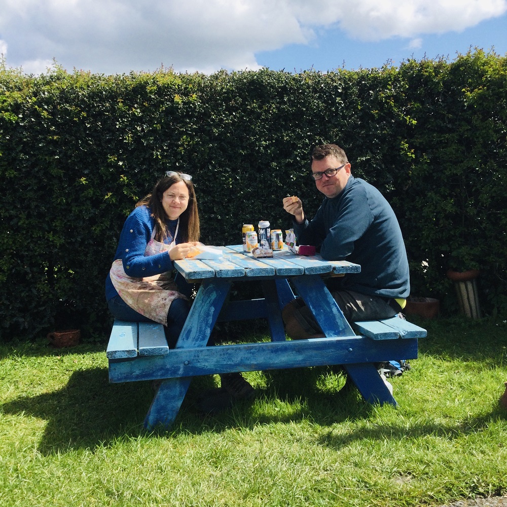 man and woman couple eating lunch on blue bench outside