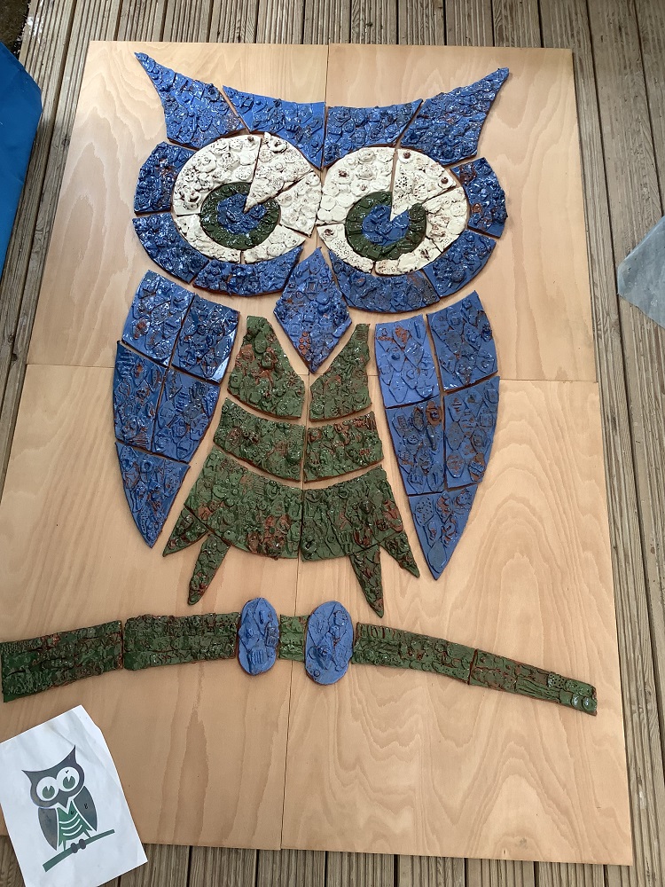 blue white and green tiles hand modeled with clay which together make up an owl 
