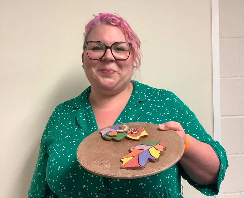 rurning point staff memeber proudly showing her oak leaf clay tiles on a circular wooden board at team building day in leominster