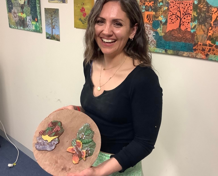 rurning point staff memeber proudly showing her oak leaf clay tiles on a circular wooden board at team building day in leominster