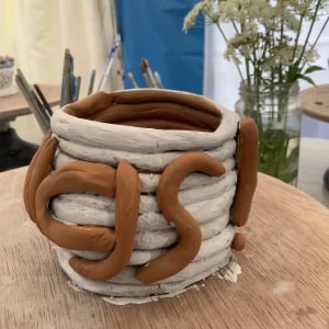 coil pot painted white with brown letters spelling part of the word 'things'