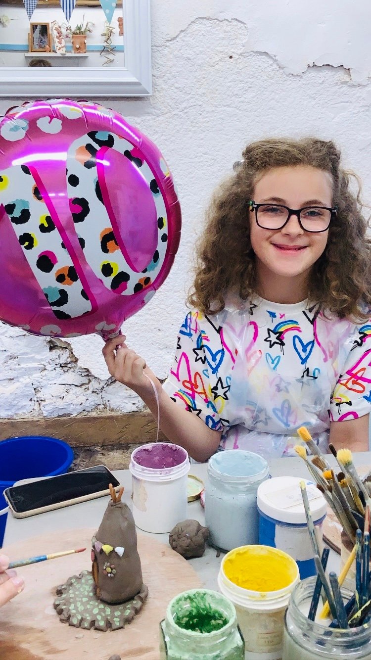child holding pink 10th birthday baloon next to clay creation made at eastnor pottery