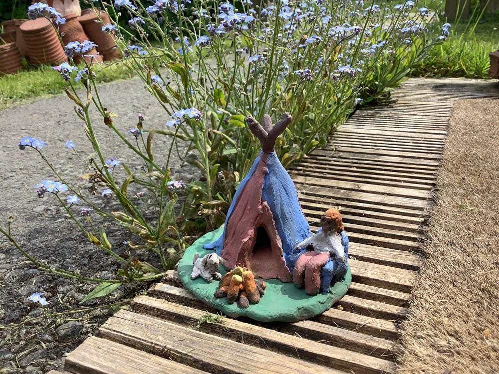 clay hand modeled tepee red and blue with person sat on a chair, fire and a white dog