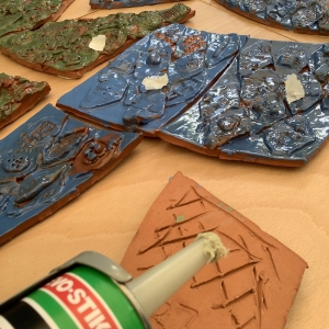 terracotta tiles painted blue and green with a glue gun tip in corner and glue on wooden surface