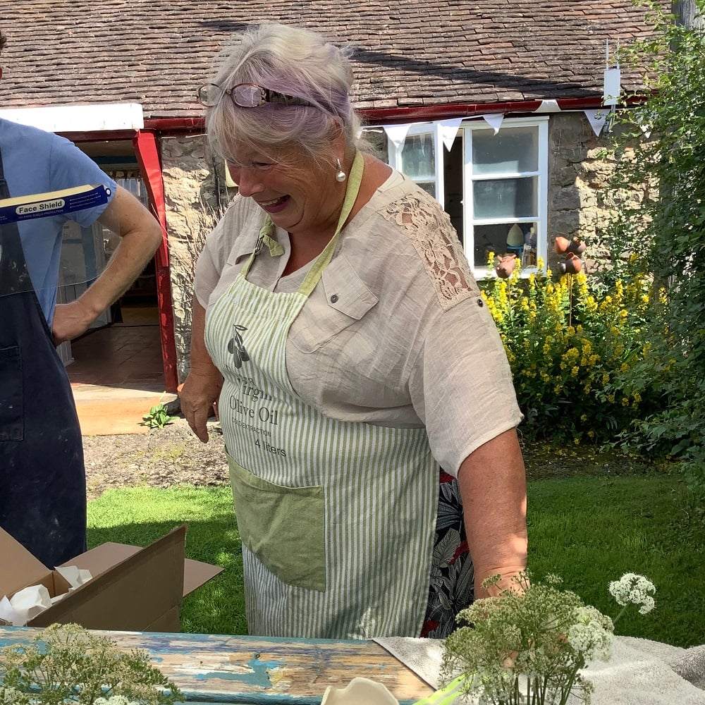 lady holding on to wooden table laughing with pottery in the background
