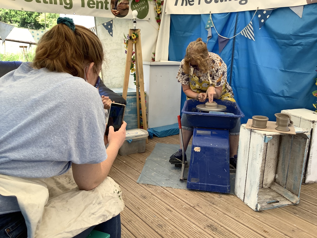 daughter filming mother on her phone whilst throwing a pot on a potters wheel