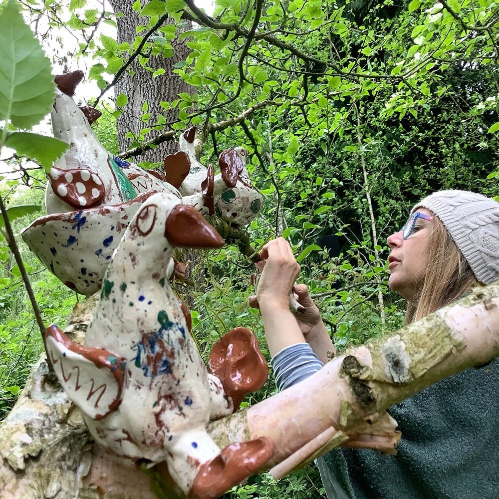 potter Sarah Monk placing ceramic birds in the trees of hellens gardens