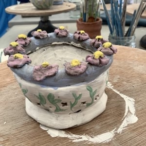 clay modelled bowl painted with with a purple rime and decorated with pink clay flowers