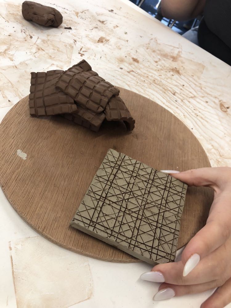 clay slabs with white slip painted on and fine straight geometric lines cut through the surface to achieve a fine wire fence effect