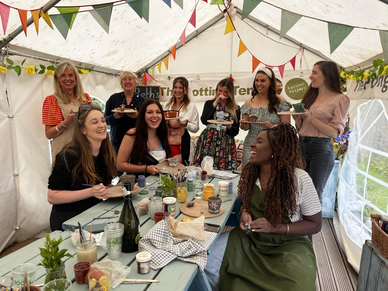 Hen Party Group gathered around the table, laughing in the potting tent at easnor pottery.