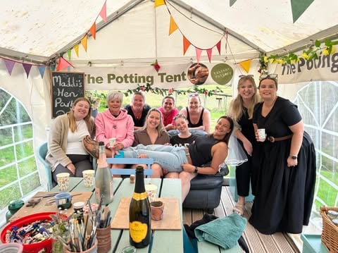 Hen Party group gathered around the sofa in the potting tent at eastnor pottery on a sunny day.