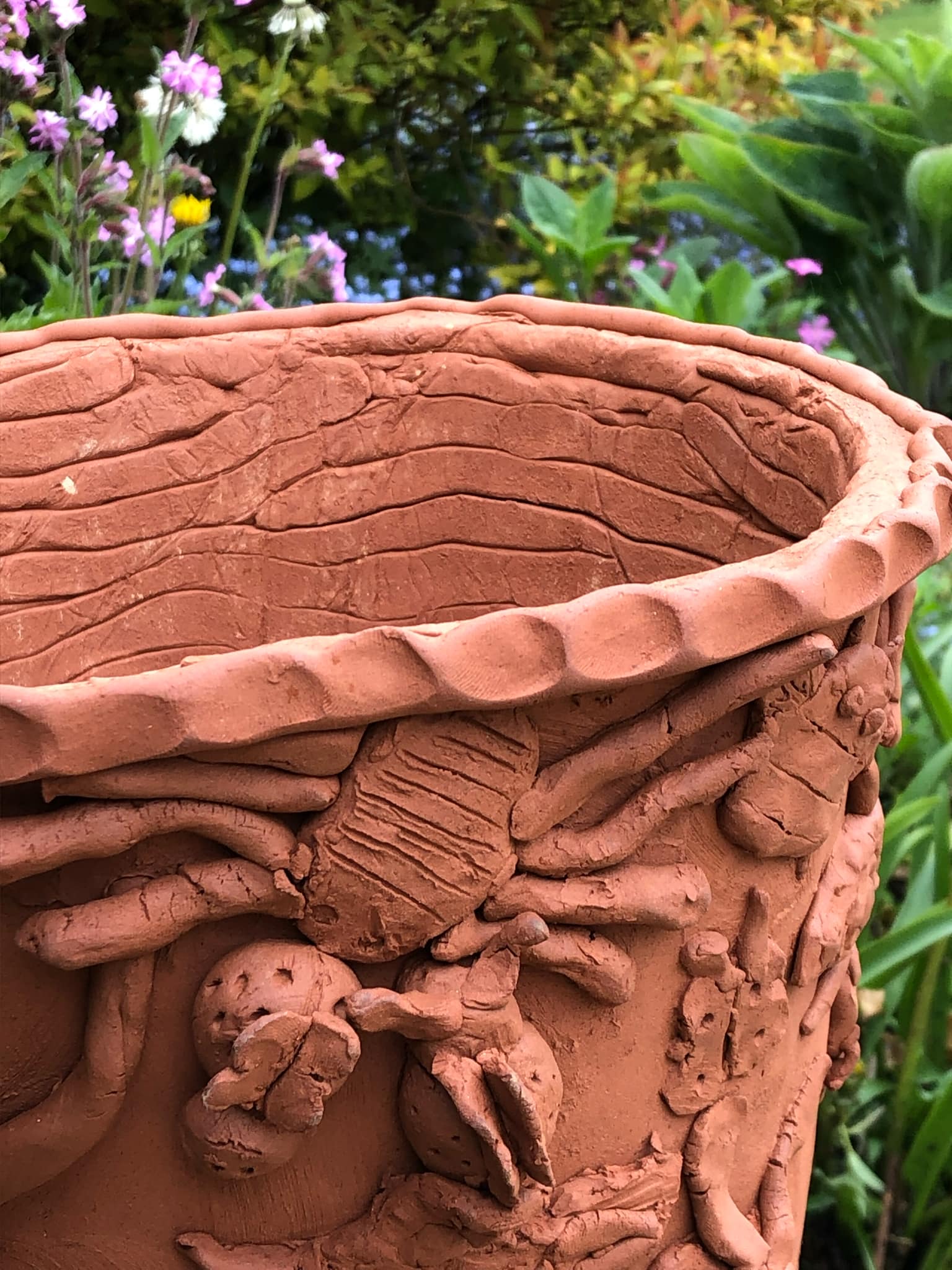 detail of large terracotta coil pot made by primary school children and exhibited at sculpture at kingham lodge exhibition. details shows a large modelled spider in low relief