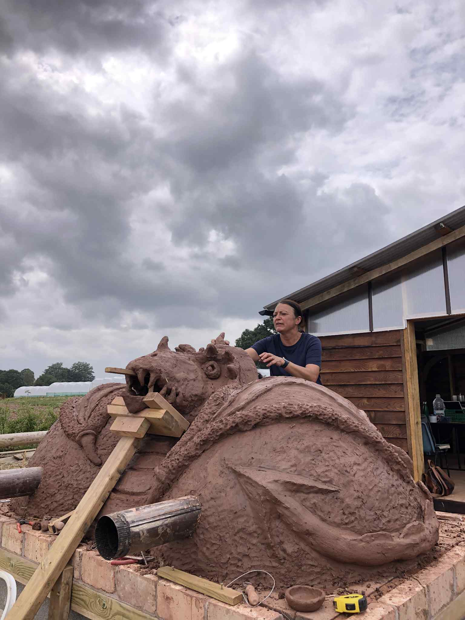 front of cob pizza oven in the shape of a dragon with it's mouth open. Dragon chin is supported by a wooden brace to prevent it from collapsing 