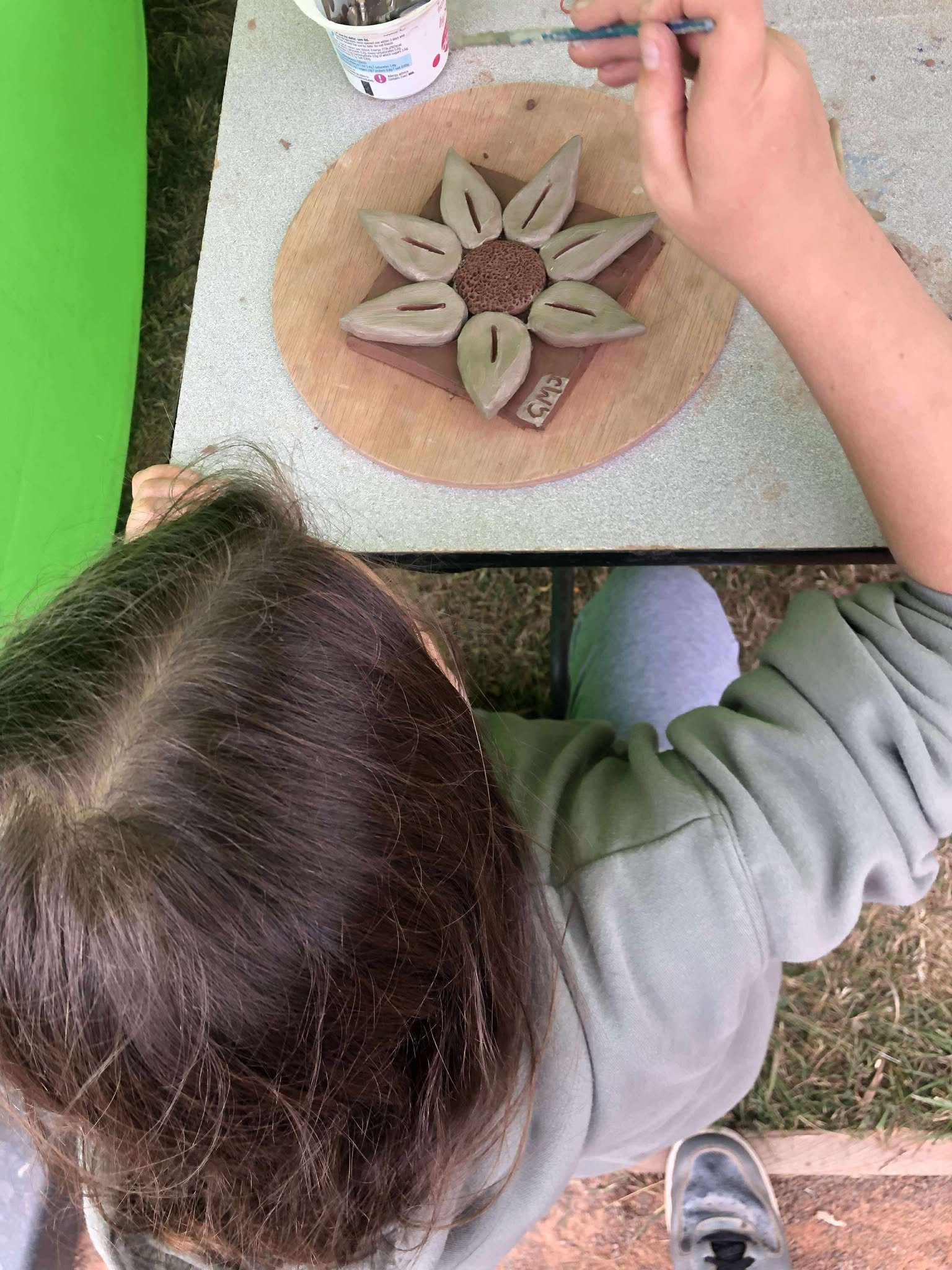 looking down at the top of a young girls head whilst she paints her modelled clay tile with white slip with a paint brush