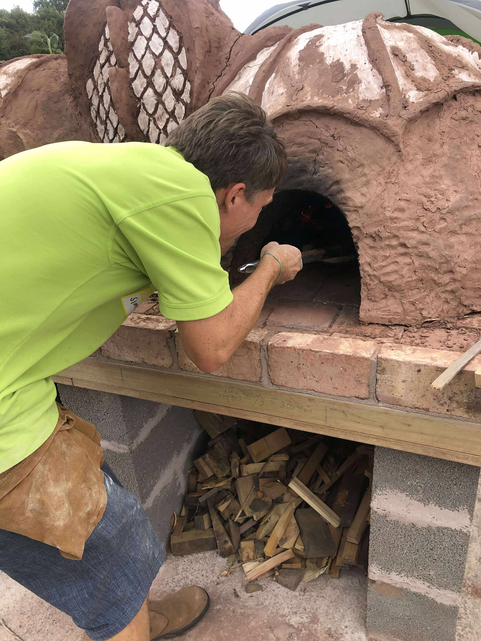 man cooking pizzas on a cob pizza oven. Using a metal padel to place the pizza into the door of the chamber. reminiscent of a cave.