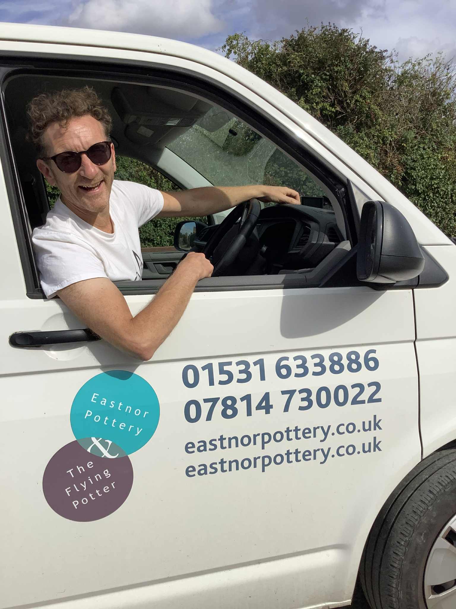 jon williams from eastnor pottery in the driving seat of his vw van sun glasses on and leaning out of the window smiling