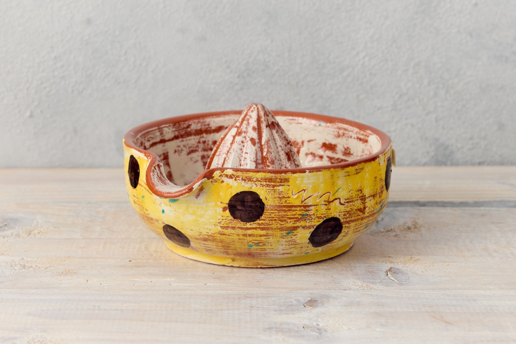 A yellow hand thrown juicer with painted dark brown dots. The inside is painted cream and terracotta Made by Sarah Monk