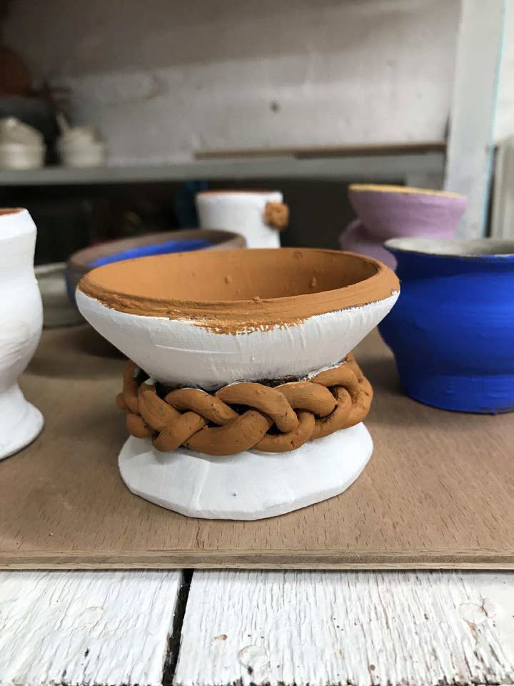 A white pot with a light brown plait wrapping around the centre of the pot.