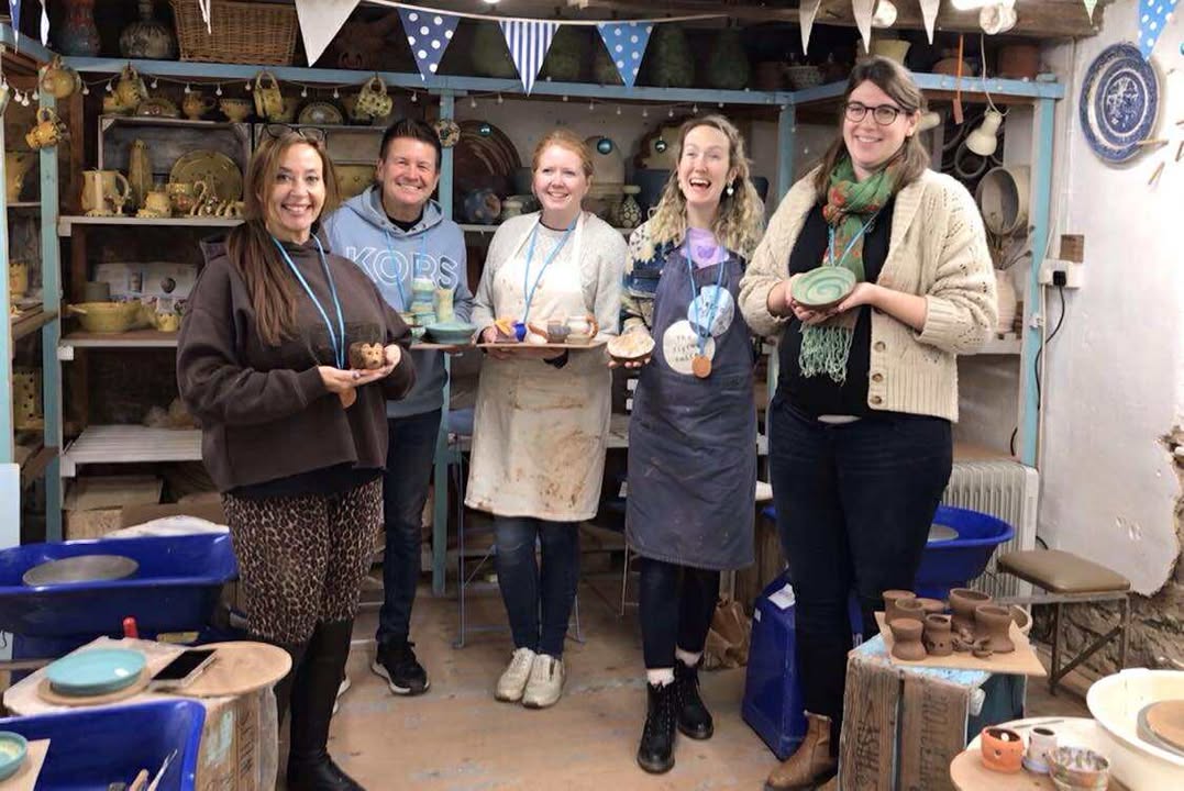 Five happy pottery course participants ! man and 4 women) stood in a row holding pots they made over the weekend. Pots include a pot modelled into a hedgehog,, a bowl with a green swirl and a splattered bowl of yellow and green.