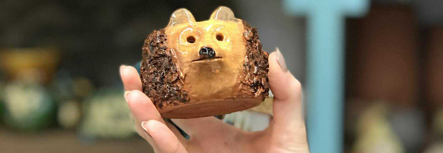 A fired and glazed pottery hedgehog pot being held up to the camera, a close up view in somebodies hand. It is approximately 10 cms in diameter.