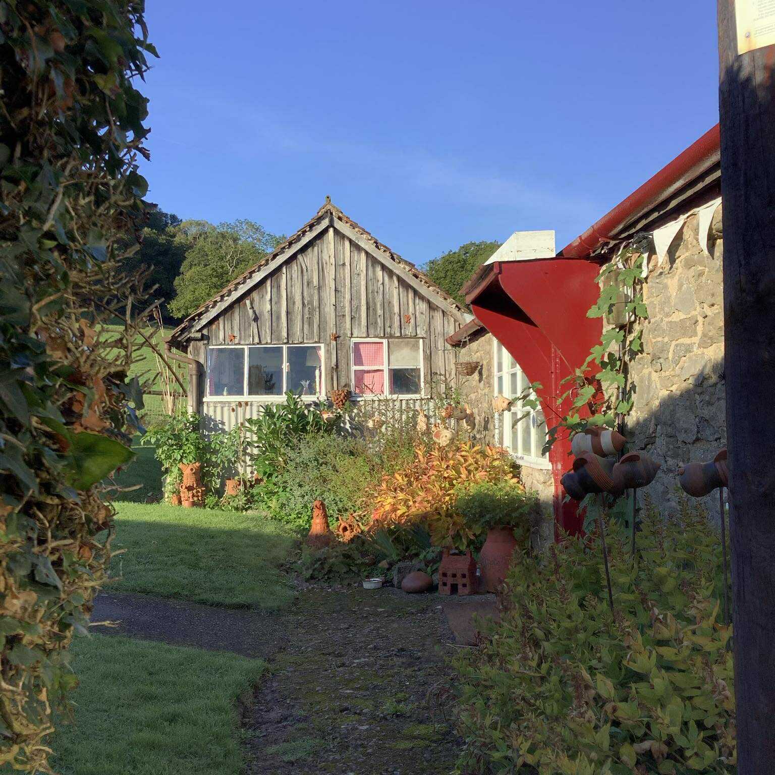 Eastnor Pottery garden shed studio shop side elevation showing corrugated iron panels below the windows and silver grey wooden panels in the apex