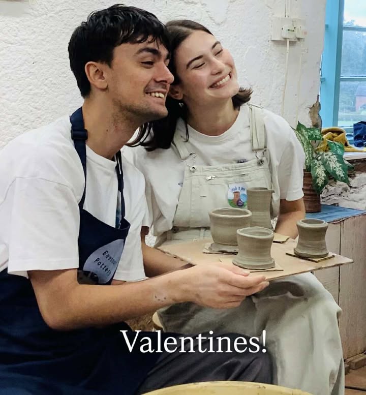 A happy young couple holding up a board of four freshly thrown pots.