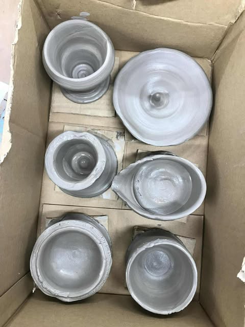 A cardboard box of freshly thrown pots, all different shapes and sizes. Some are straight, some are wobbly.