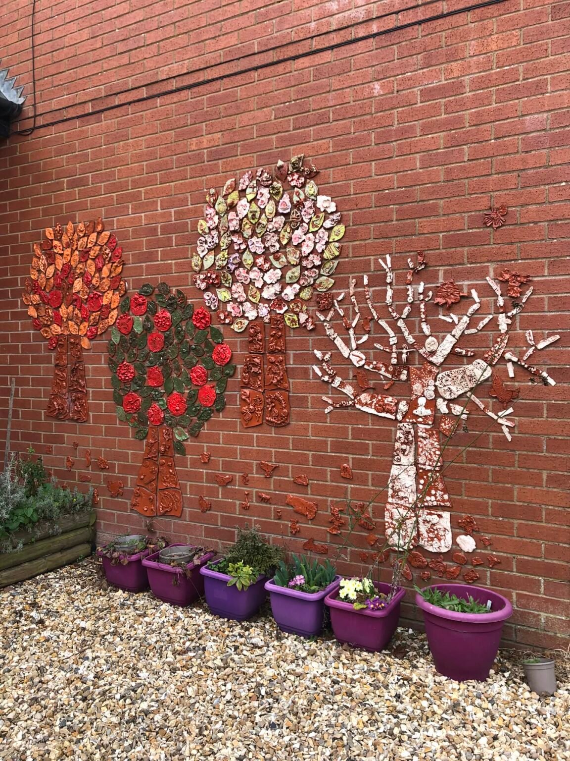 Four pottery trees mounted on the exterior wall of Ivington Primary School in Herefordshire. Each tree represents an individual season. From left to right we have autumn summer spring and winter. It was created by jon the potter from eastnor pottery and all the children and staff at Ivington Primary school