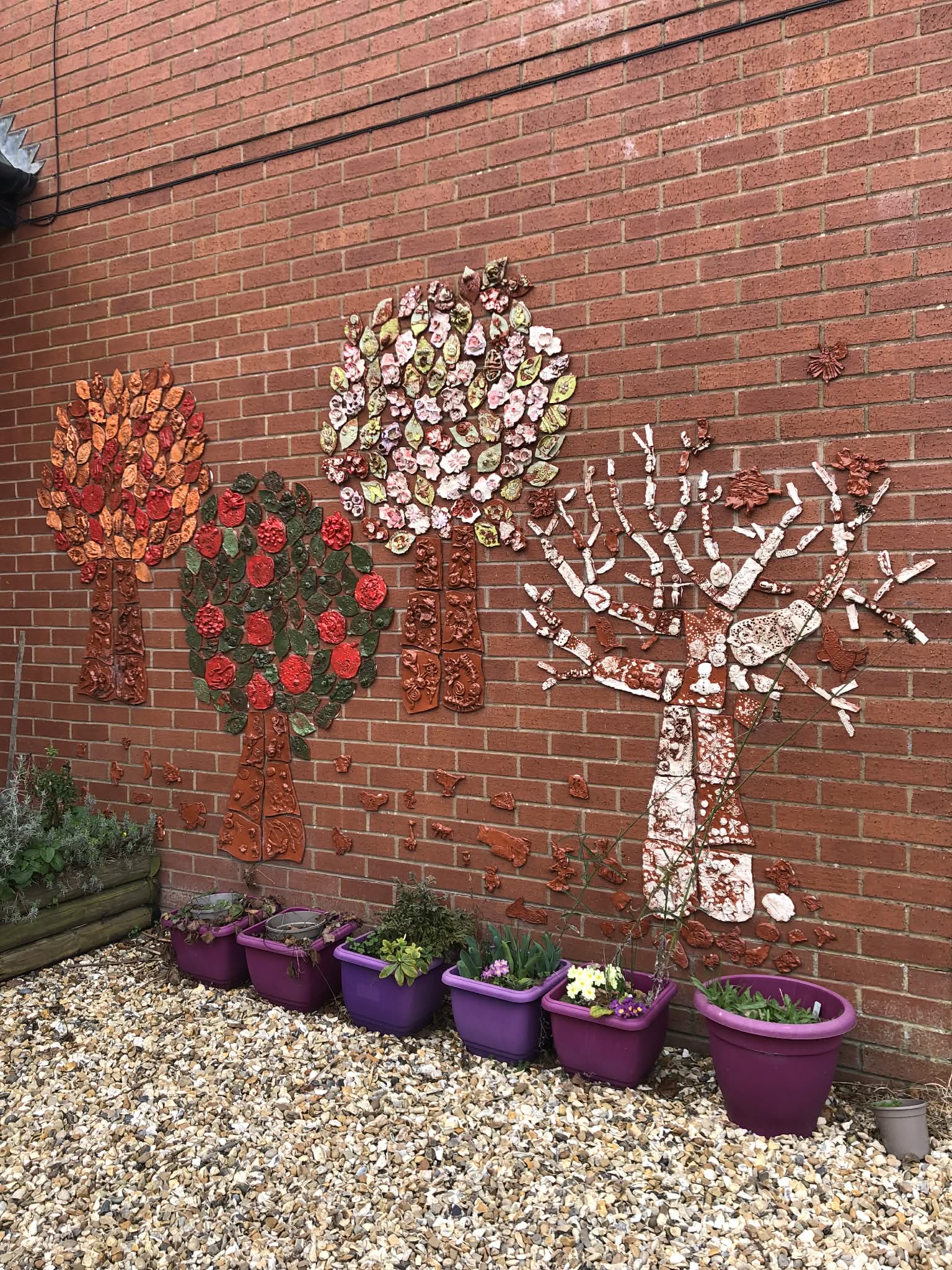 Four pottery trees mounted on the exterior wall of Ivington Primary School in Herefordshire. Each tree represents an individual season. From left to right we have autumn summer spring and winter. It was created by jon the potter from eastnor pottery and all the children and staff at Ivington Primary school