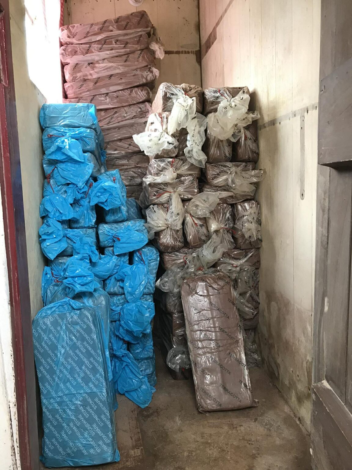 The clay store at eastnor pottery. Blue bags are stacked on the left and brown bags on the right. There are x60 bags stacked on top of each other.