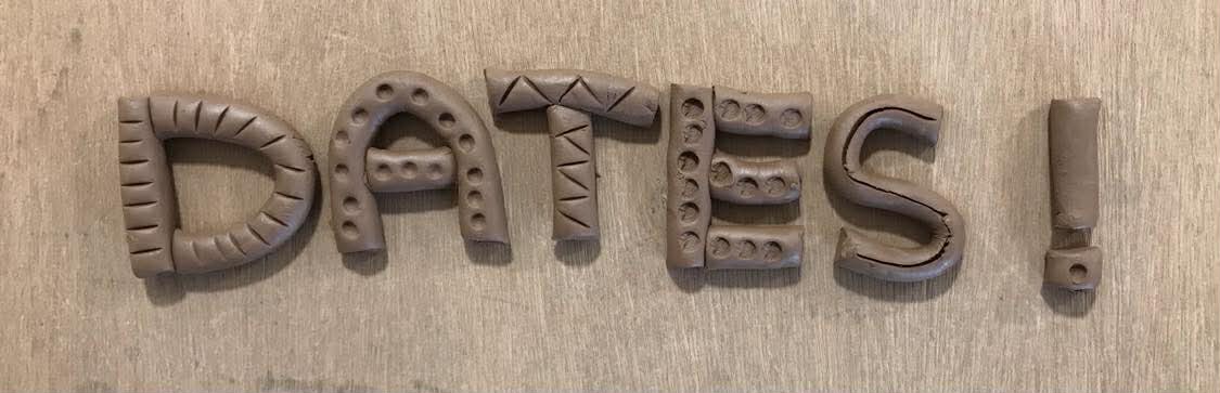 The word DATES with an exclamation mark made out of rolled terracotta clay and indented with dots and stipes. It is arranged on a wooden table top