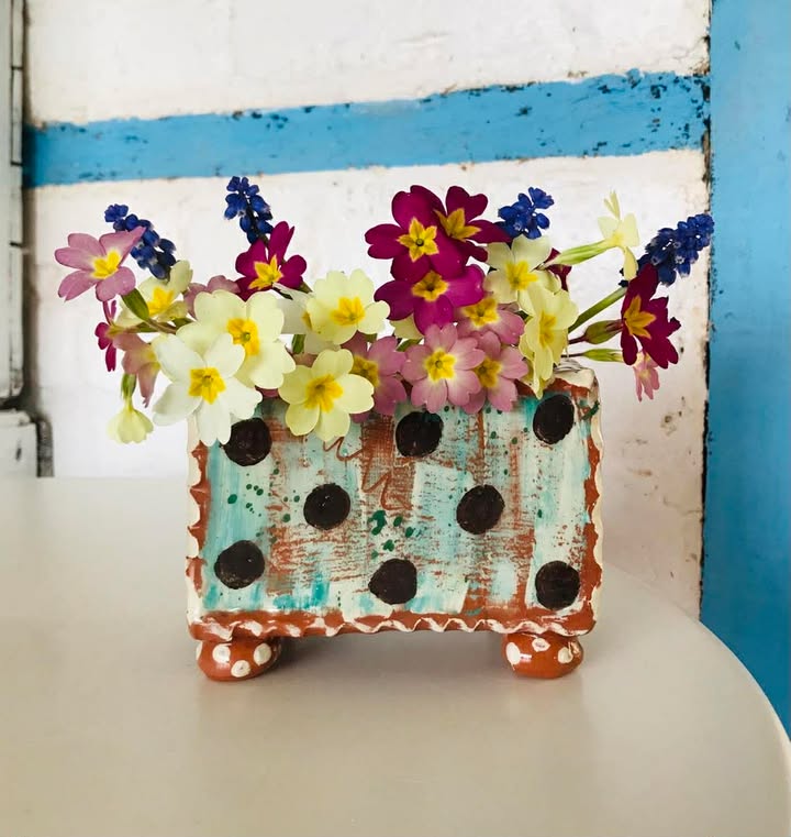 A teal rectangular flower brick with dark brown dots full of colourful fresh primroses.