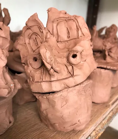 clay canopic jar made from brown terracotta clay with a large lid in the shape of a falcon made by a YR 3 student at charlton kings junior school in cheltenham. The pot features a beak in the middle of two googly eyes and two large ears