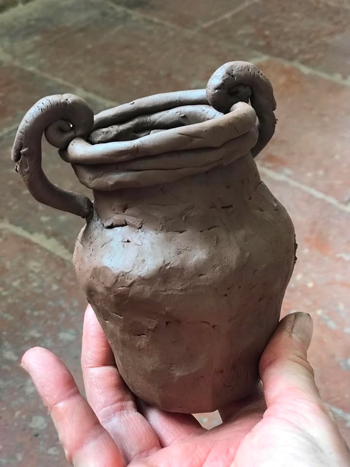 A terracotta clay pot held in hand. The pot is a traditional amphora shape with a high shoulder and curly handles.