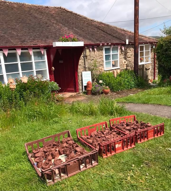 Three plastic 'bakery' trays full of children's pottery drying on the grass outside Eastnor Pottery.