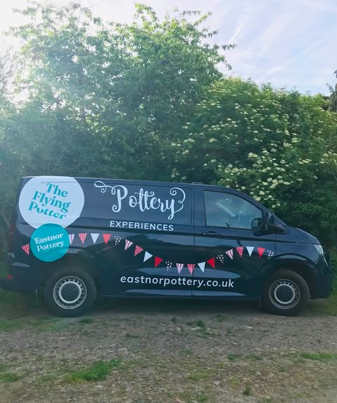 A dark blue VW Van with large stickers on the side: there's bunting, the words pottery experiences, the flying potter,and eastnor pottery.