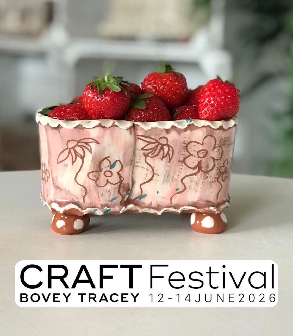 A ceramic oval fruit punnet, pink wit a white pie crust rim and etched sgraffito flowers. There are some fresh strawberries inside it. There is a graphics banner below which says Craft Festival , Bovey tracey. 12-14 June 2026