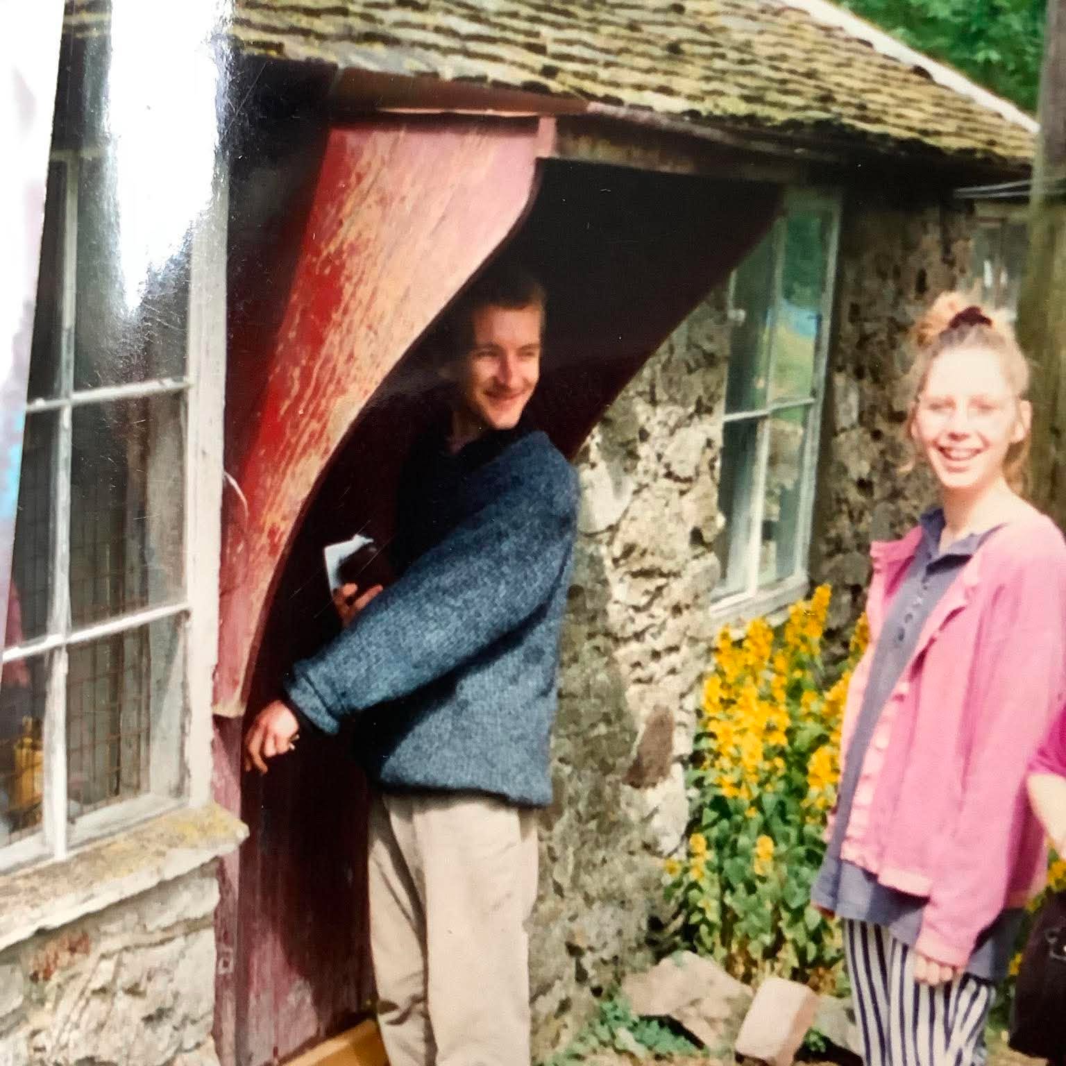 Jon Williams and sarah monk opening the door of their studio in eastnor for the very first time. Sarah, in a pink jacket is looking at the camera whilst jon who is opening the door is smiling at sarah. Its a warm sumnny day and there are yellow flowers in bloom in the flower border