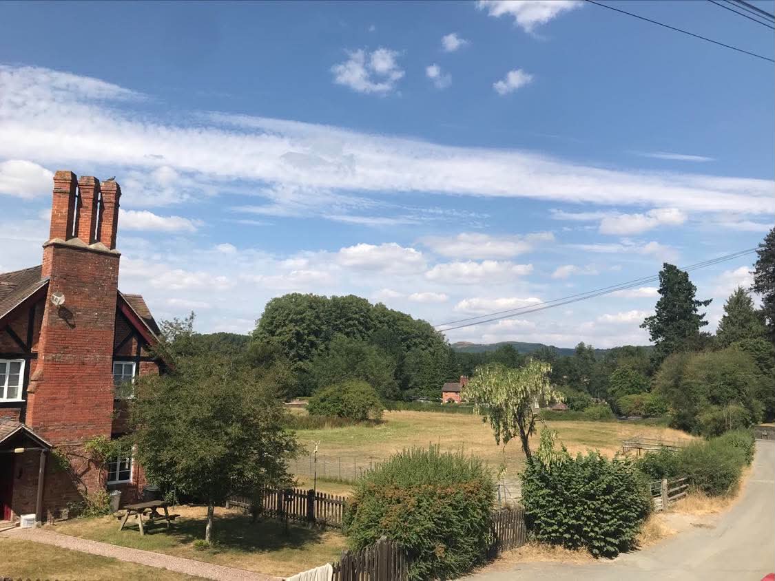 The view from the exterior steps at Eastnor Pottery overlooking the red bricks and black beams of Eastnor Castle Estate Office - a side elevation displaying a large chimney breast and three impressive chimney pots pointing skyward.