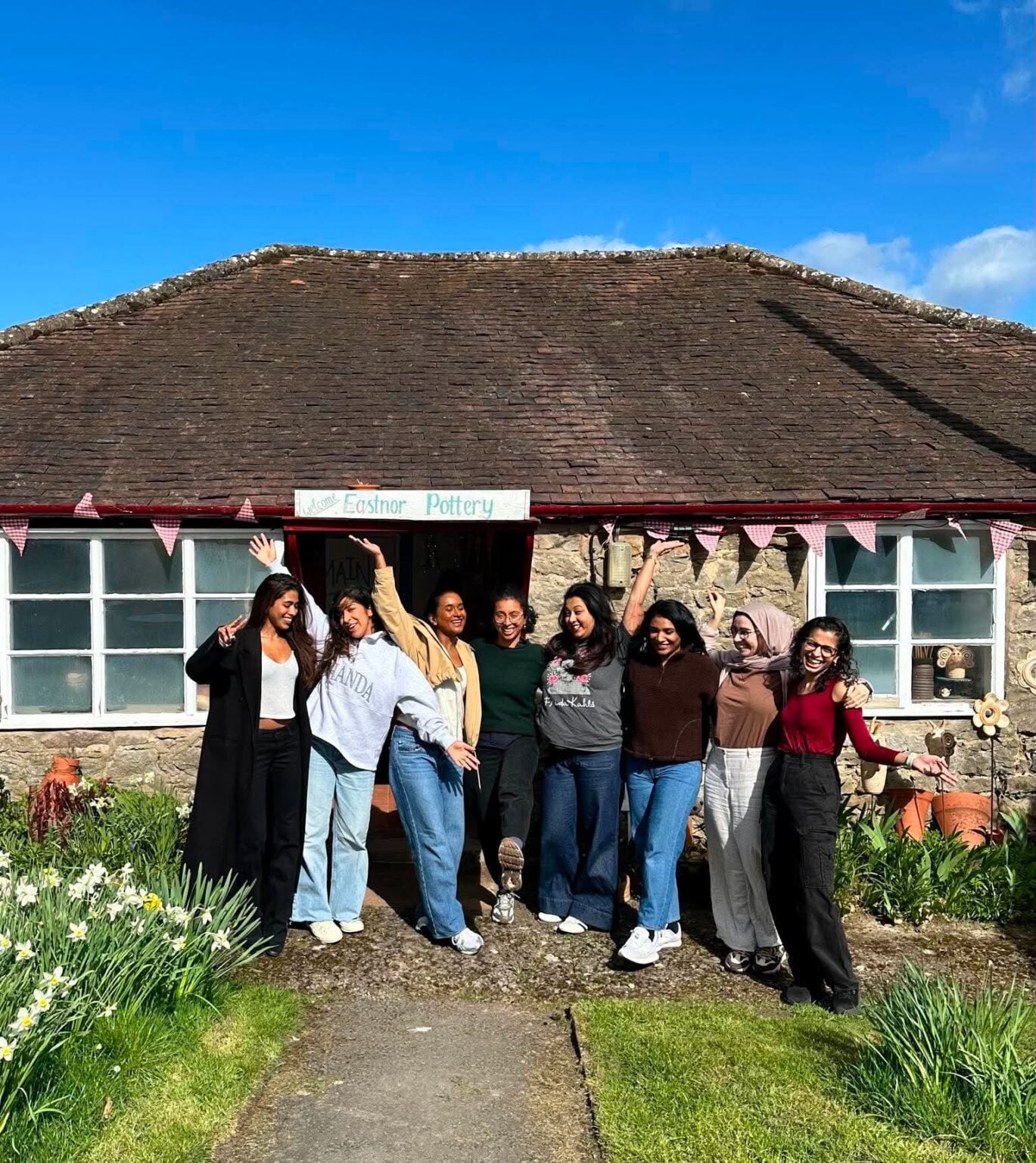 A group of 8 girls stood together outside the studio. They are laughing and posing at the camera in a cheerful manner.