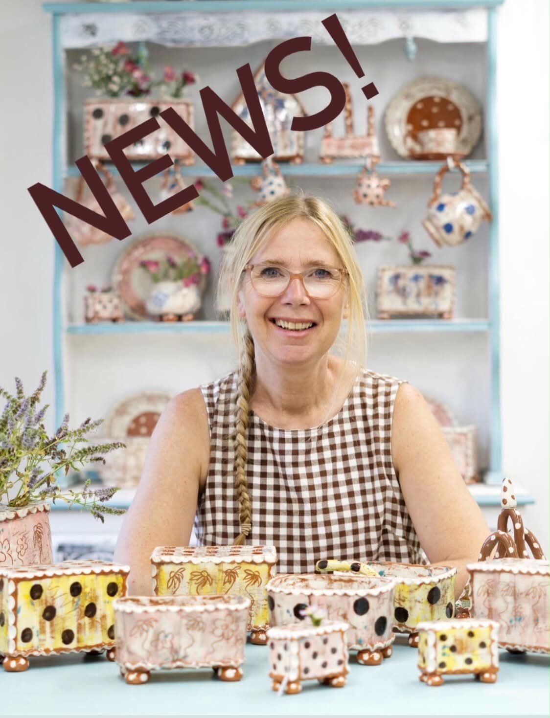 A smiling lady with blond hair and pink glasses with a side plait wearing a checked cotton t-shirt. She is sat behind a table with lots of colourful pottery in front of her and behind her. The word NEWS! has been added to the picture.